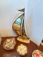 Metal sailboat sculpture next to baskets and bag of seashells