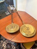 Pair of brass bed warmers with wood handles on table