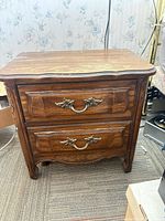 Front view of one nightstand showing two drawers, ornate pull handles, carved legs