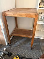 Full view of one wooden side table showing top, legs, lower shelf, and casters