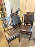 Front view of four folding chairs showing slat backs and padded seats