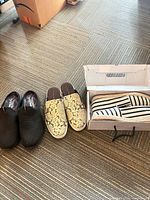 All three pairs lined up: black knit slip-ons, snake print mules, striped espadrilles in box