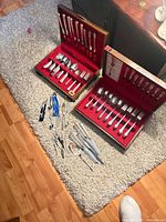 Two wooden flatware cases open showing knives, spoons, forks; loose utensils on carpet