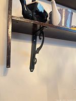 View of lower shelf underside and one scroll metal bracket with partial teapot shapes visible
