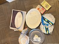 Lot overview showing platter in box, disposable plates, forks, doilies, napkins