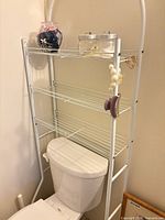 Full view of white metal over-toilet rack with three shelves