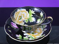 Cup resting on saucer showing floral pattern, gold rim, black glaze