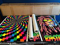 Two unrolled posters (psychedelic spiral and Rasta lion) with three rolled posters on table