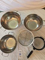 Top view of three bowl colanders, round mesh strainer and handheld mesh strainer