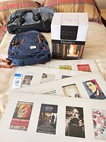 Backpack, one grey duffel, boxed fireplace and stacked matted prints on bed