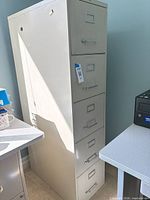 Full view of beige 5-drawer vertical metal filing cabinet beside desk