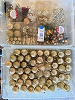 View of stacked clear bins containing gold ball ornaments, tree topper, picks, birds and accessories
