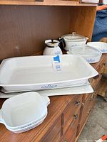Overall view showing large dish on metal rack, tray beneath, coffee pot, covered casserole