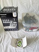Group shot showing Panasonic phone system box, plastic bin of chargers and batteries, and boxed iPod Shuffle with earbuds