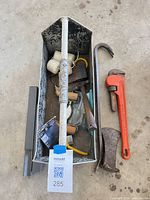 Overview of all tools in metal tray with pipe wrench and pry bar