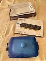 Lot overview showing boxed trays, boxed muffin pan, blue casserole with lid