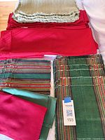 Overview of stacked green fringed placemats, red tablecloth/runner, striped placemats, solid napkins