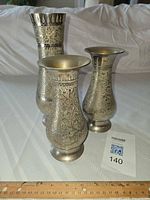 Three silver-plated engraved vases standing with ruler for scale