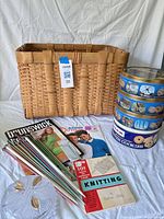 Overview of basket, knitting needles, pattern books, cookie tins, glass dish