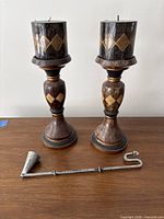 Two matching diamond-pattern candle holders with candles and snuffer on table