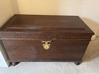 Closed cedar chest showing carved trim, brass hardware, bun feet