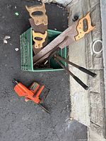 Crate containing hand saws, rasp, loppers with chainsaw in foreground