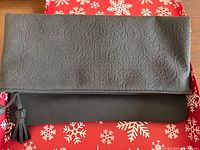 Front view of black embossed fold-over clutch showing paisley pattern and tassel zipper pull