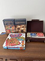 Group shot showing Traditions Snakes and Ladders, Traditions Checkers, Hasbro Guess Who? and leatherette case with cards and dominoes