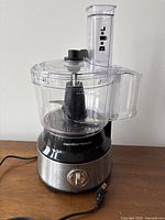 Front view of Hamilton Beach food processor showing brand badge, clear bowl and lid