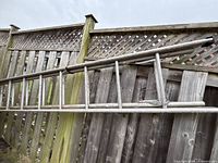 Full view of one aluminum ladder leaning on fence