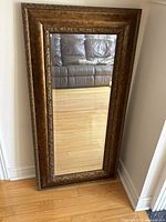 Front view of rectangular gold-tone framed mirror leaning against wall