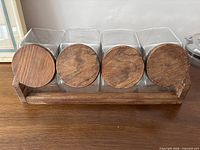 Front view of four glass canisters with wooden lids seated in wooden rack