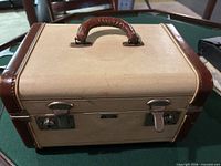 Front view of cream and brown makeup case showing top handle and dual latches