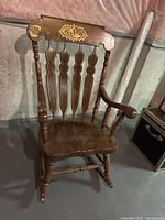Front three-quarter view of wooden rocking chair showing spindle back, seat, arms, gold stencil on crest rail