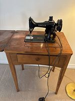 Singer sewing machine mounted in cabinet, cords visible