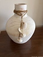 Front view of off-white ceramic vase with rope and shells