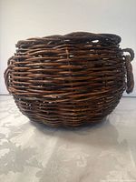 side view of brown round wicker basket with loop handles