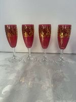 Front view of four ruby red liqueur glasses in a row showing gold bands