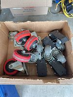 box containing assorted red and grey swivel casters and black plates
