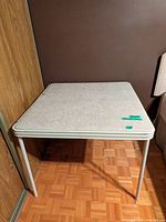 Square vinyl-top card table positioned against wall