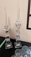 Two clear glass candlesticks with taper candles; edge of floral bowl visible