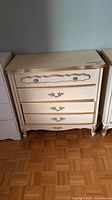 Front view of cream dresser showing four drawers, gold trim, decorative pulls