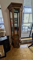 Full view of tall oak glass curio cabinet beside window