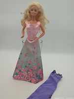 Full view of Barbie doll wearing floral dress, extra purple dress in foreground
