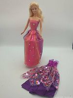 Full view of Barbie doll standing with additional purple sequin dress laid beside