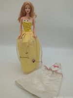 Full view of Barbie doll wearing yellow gown, white gown laid beside