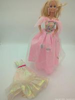 Full view of Barbie doll wearing pink Butterfly Princess dress with extra iridescent dress laid beside