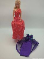 Full view of Barbie doll in red dress beside purple wrap