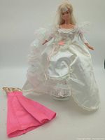 Full view of Barbie in bridal gown with extra pink gown beside stand