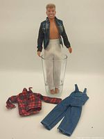 Full view of doll standing in glass plus extra clothing pieces